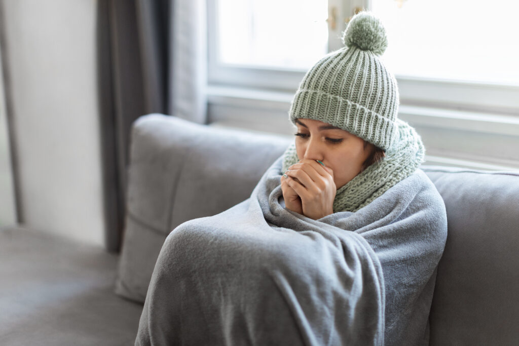 Young Woman Feeling Cold At Home, Sitting On Couch Covered In Blanket